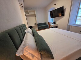 Quarto de hotel com cama, sofá verde, escrivaninha com cadeira, televisão e janela.