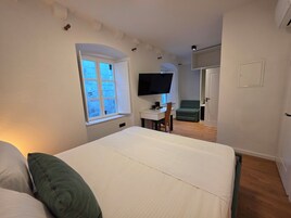Quarto com cama, escrivaninha, televisão e uma cadeira verde.