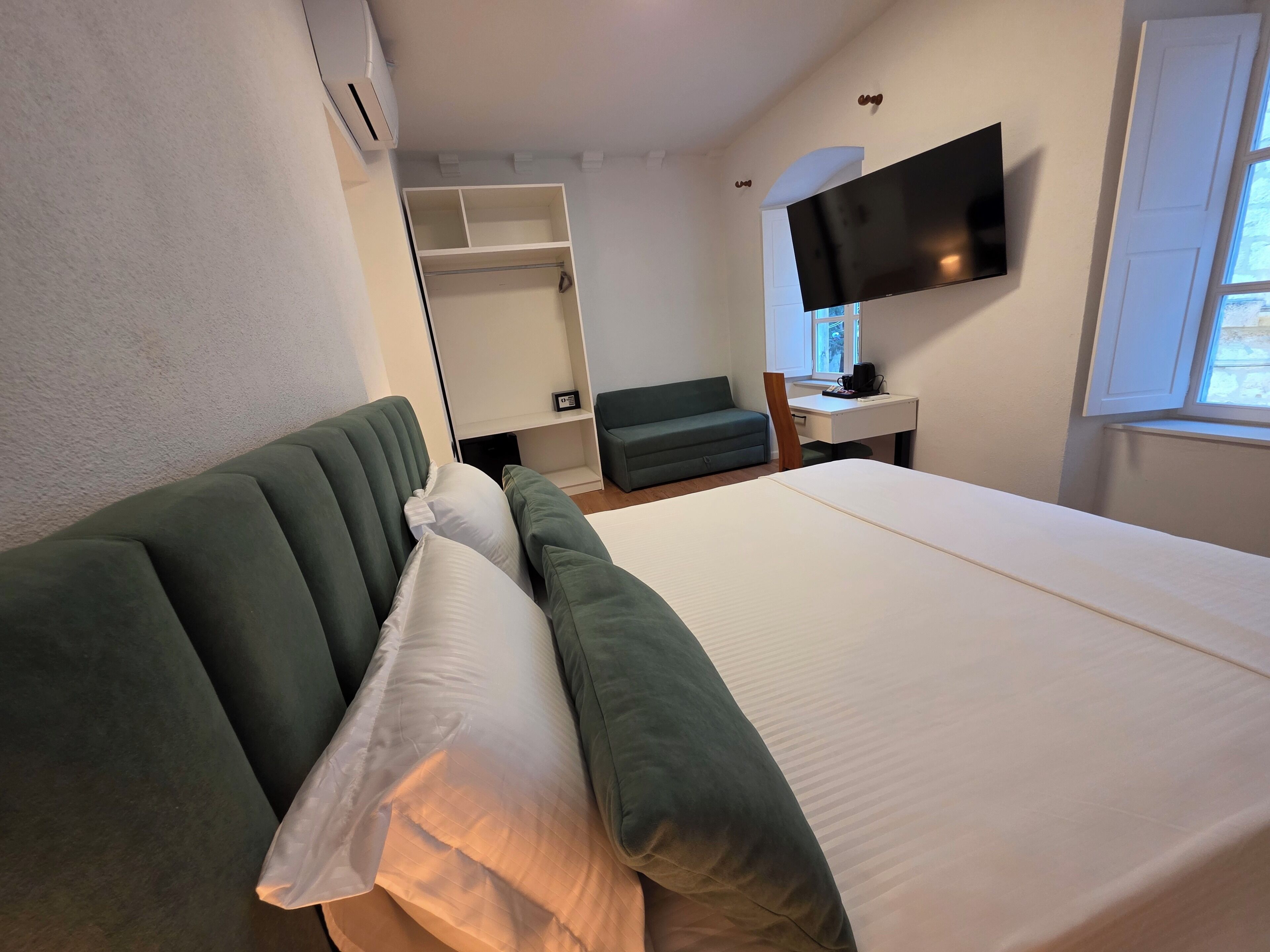 Et hotelværelse med en seng, en grøn sofa, et skrivebord med et fladskærms-tv og et vindue.