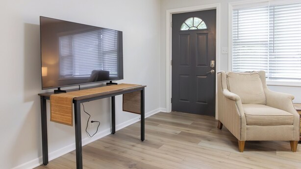 A room with a television on a wooden table, a door, and a chair. - Entire Hobart Home (Hobart)