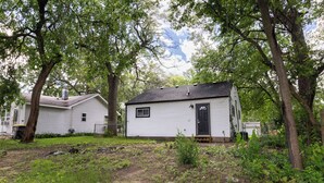 A small, single-story house with a dark roof and white siding, surrounded by trees and overgrown vegetation. - Entire Hobart Home (Hobart)