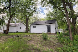 A small, single-story house with a dark roof and white siding, surrounded by trees and overgrown vegetation. - Entire Hobart Home (Hobart)