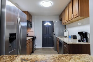A kitchen with stainless steel appliances, wooden cabinets, a dark door, and a countertop with a coffee maker. - Entire Hobart Home (Hobart)