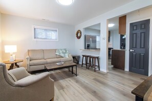 A living room with a sofa, coffee table, and chairs, a kitchen area with a refrigerator, and a door leading to another room. - Entire Hobart Home (Hobart)