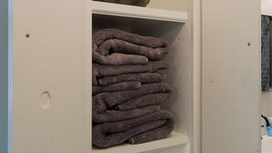 A bathroom with a white door, a towel rack with folded towels, and toilet paper on the lower shelf. - Entire Hobart Home (Hobart)