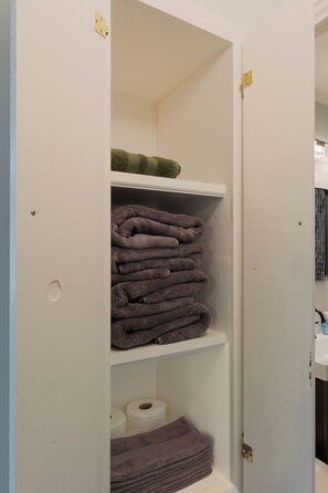 A bathroom with a white door, a towel rack with folded towels, and toilet paper on the lower shelf. - Entire Hobart Home (Hobart)