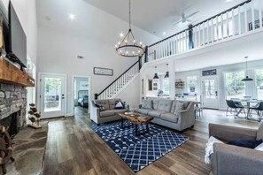 Ein geräumiges Wohnzimmer mit Kamin, einer Treppe zu einer oberen Ebene und einem Essbereich mit moderner Einrichtung.