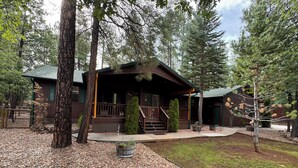 A lodge with a porch, a stone pathway, and a forested backdrop. - Adorable 3-bedroom cabin in Pinetop Country Club, newly renovated. Pets Welcome! (Pinetop Country Club)