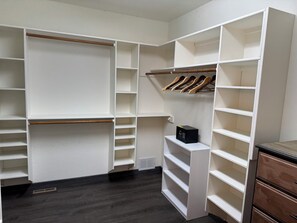Ein begehbarer Kleiderschrank mit mehreren Regalen und Ablageflächen, einem Lüftungsgitter und einer kleinen Schachtel auf einem Regal.