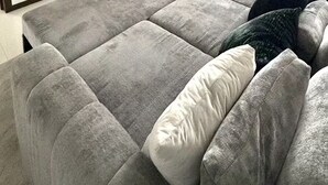 Ein Wohnzimmer mit einem großen grauen Sofa, einem flachbildfernseher an der Wand und einem Fenster mit Jalousien.