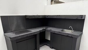 Eine kleine Küche mit Spüle, Grill und dunklen Schränken.