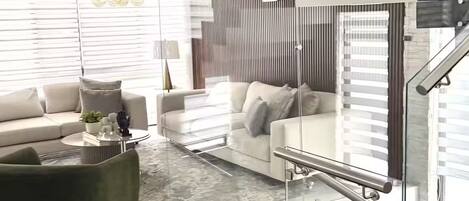 Ein modernes Wohnzimmer mit Wendeltreppe aus Glas, einer Couch, einem Couchtisch und einem Kronleuchter.