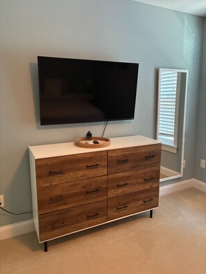 A room with a large flat-screen TV mounted on the wall, a wooden dresser with drawers, and a window with blinds. - Casa Sul Lago Spacious 5-bedroom house in charming Delavan w/AC Firepit Deck (Delavan)