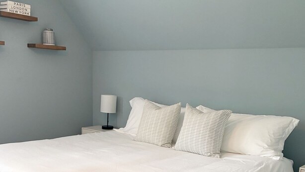 A bedroom with a large bed, a nightstand, a lamp, and a wall-mounted shelf with books. - Casa Sul Lago Spacious 5-bedroom house in charming Delavan w/AC Firepit Deck (Delavan)