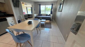Cocina compacta con una mesa de comedor y sillas, un sofá y un ventanal con cortinas.