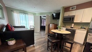 Un espacio habitable compacto con kitchenette, comedor y dormitorio con cama y mesita de noche.