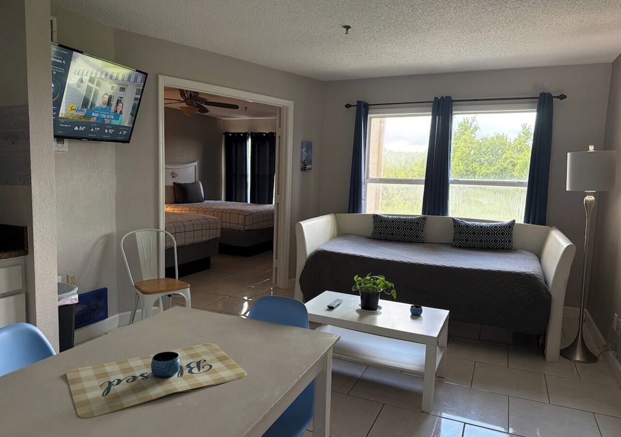 A cozy room with a bed, a sofa, a dining table, and a TV mounted on the wall.