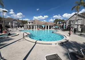 A swimming pool area with multiple pools, lounge chairs, and a fenced perimeter. - Lyrios Vacation Rentals - The Palms (Kissimmee)