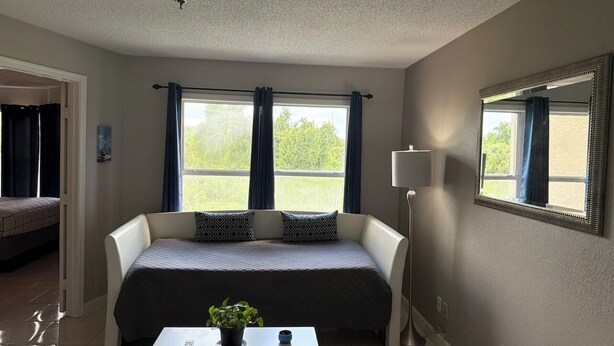 Una habitación con una cama, una mesa con una planta, una lámpara y un ventanal con cortinas.