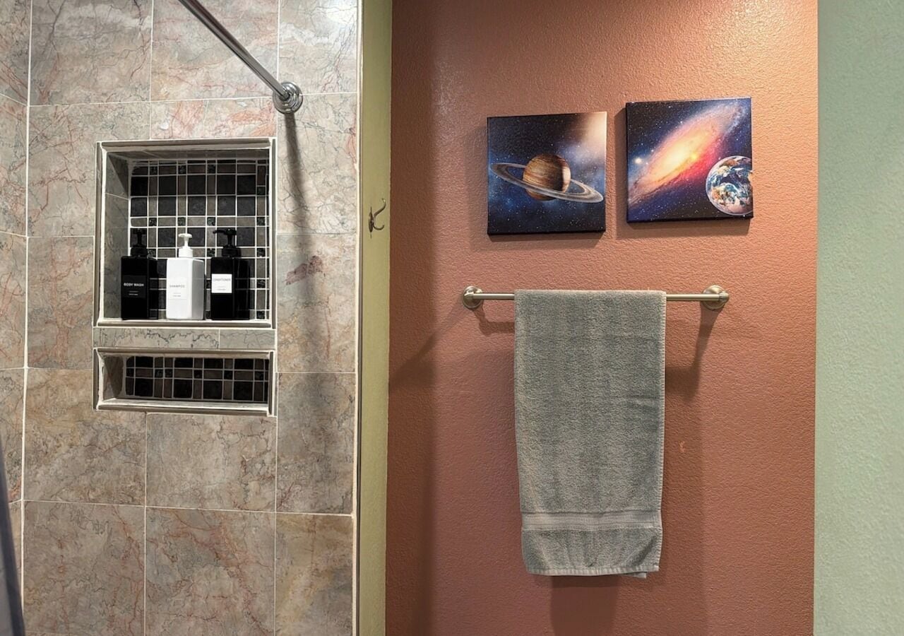 A bathroom with a shower, a towel rack, and two space-themed wall art pieces.