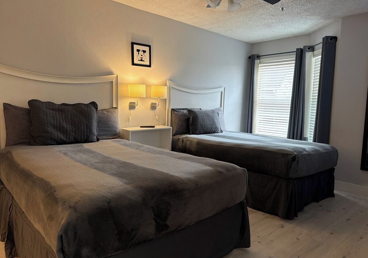Ett hotellrum med två sängar, ett nattduksbord, en lampa och ett fönster med gardiner.