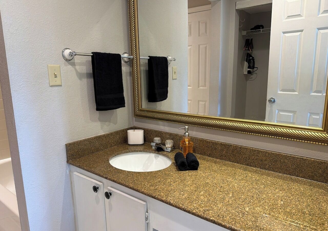 Une salle de bain avec un lavabo blanc, un miroir à cadre doré et un porte-serviettes avec deux serviettes.