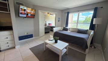 Un dormitorio con cama, televisor montado en la pared, escritorio y ventana con cortinas.