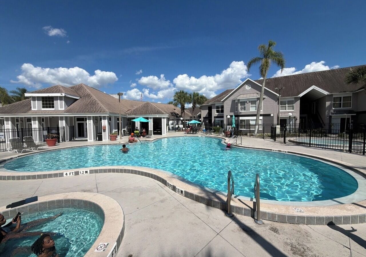 A swimming pool with a curved design, surrounded by a paved deck and a fence.