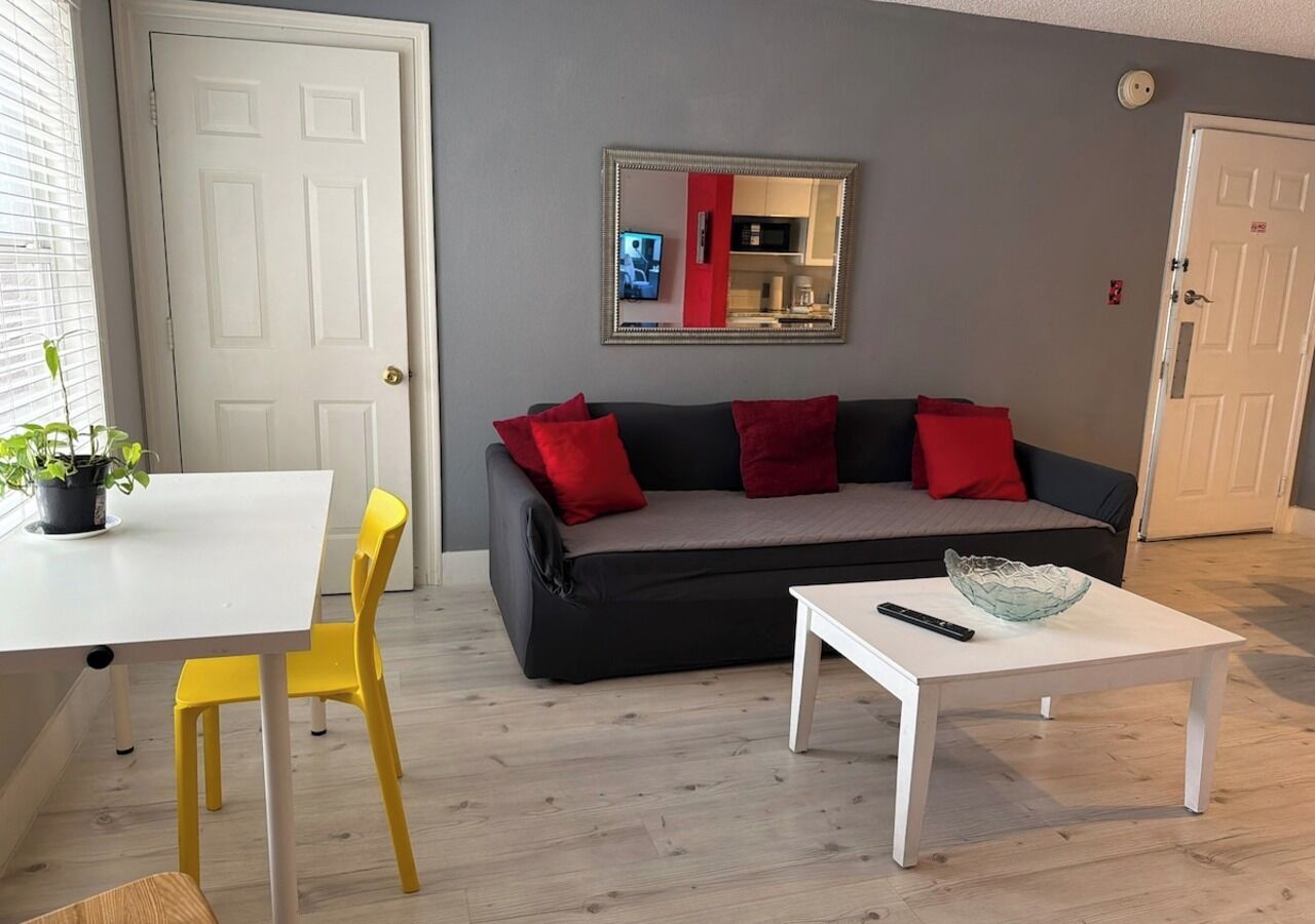 Una sala de estar con un sofá, una mesa de comedor con sillas, una mesita de centro y un espejo en la pared.