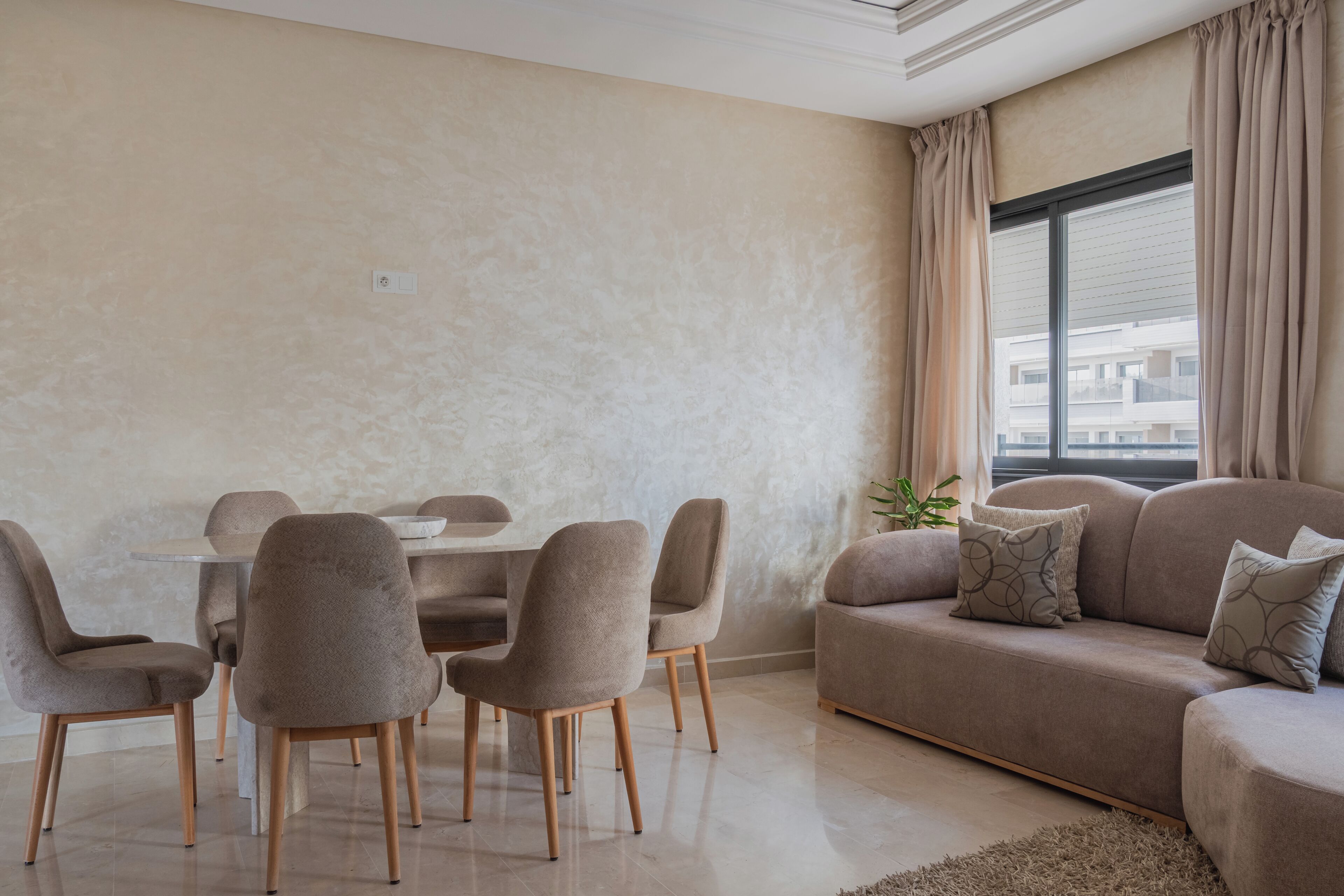 Een moderne woonkamer met een eettafel, stoelen, een bank en een groot raam met gordijnen.