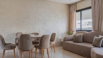 Een moderne woonkamer met een eettafel, stoelen, een bank en een groot raam met gordijnen.