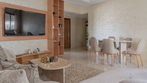 Un soggiorno moderno con una TV a schermo piatto, una libreria in legno, un'area pranzo con sedie e un divano.