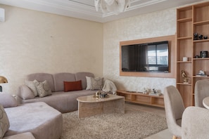 A modern living room with a sofa, coffee table, and a TV mounted on the wall. - Stunning New 3BR/2BA | Steps to TGV Station, Hilton & Tangier Corniche (Tanger)