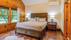 A bedroom with a wooden bed, two bedside tables with lamps, a window with curtains, and an air conditioning unit. - Jay Brook Lodge | Sleeps 16 | Hot Tub | Game Room (Jay)