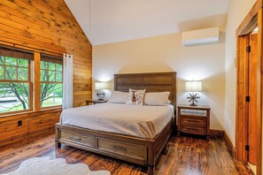 A bedroom with a wooden bed, two bedside tables with lamps, a window with curtains, and an air conditioning unit. - Jay Brook Lodge | Sleeps 16 | Hot Tub | Game Room (Jay)