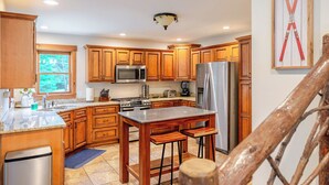 A kitchen with wooden cabinets, stainless steel appliances, and a large window. - Jay Brook Lodge | Sleeps 16 | Hot Tub | Game Room (Jay)