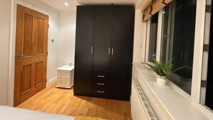 A bedroom with a wardrobe, a bedside table, a window with a plant, and a radiator. - Modern and super cosy apartment, peaceful location, Richmond London (Richmond)