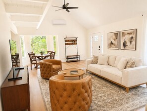Ein geräumiges Wohnzimmer mit hoher Decke, einem Deckenventilator, einer Couch, einem Couchtisch und einem Essbereich mit Stühlen und einem Tisch.