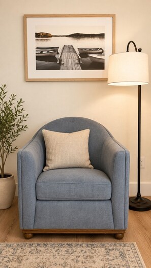 Ein blauer Sessel mit Kissen, eine Stehlampe, ein gerahmtes Foto an der Wand und ein Blumentopf.