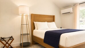 Una camera da letto con un letto in legno, biancheria da letto bianca, una coperta blu, una lampada da terra e una lampada da piedistallo.