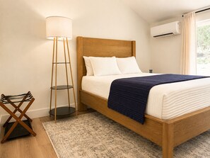 Ein Schlafzimmer mit einem hölzernen Bett, weißer Bettwäsche, einer blauen Decke, einer Stehlampe und einer Stehlampen.