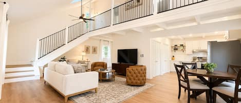 A spacious living area with a staircase, a dining table, and a kitchen in the background.