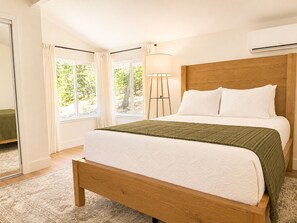A bedroom with a wooden bed, white bedding, a floor lamp, and large windows with curtains. - The Mountain Getaway Near Apple Hill with Private Lakes, OHV Trails, & Airstrip (Placerville)