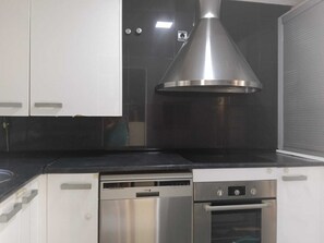 Una cuina amb armaris blancs, una campana extractora d'acer inoxidable, un rentaplats i un forn.