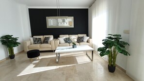 Ein modernes Wohnzimmer mit einem beigen Sofa, einem weißen Couchtisch und zwei Zimmerpflanzen.