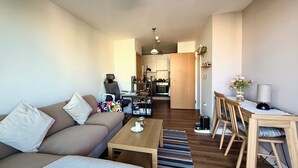 Una sala moderna con sofá, mesa de centro y comedor con sillas y una mesa. Se ve una cocina al fondo.