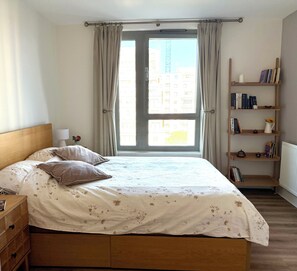 Ein Schlafzimmer mit einem Bett, einem Nachttisch, einem Bücherregal und einem Fenster mit Vorhängen.