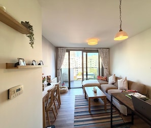 Ein modernes Wohnzimmer mit Sofa, Couchtisch und Essbereich. Ein Balkon bietet Blick auf Gebäude.