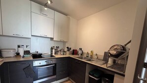 Cocina moderna con horno empotrado, estufa y lavamanos. Hay un cubo de basura y una cafetera en la encimera.