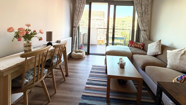 Una sala moderna con un sofá, una mesa de comedor y una silla. Se ve un balcón con barandilla.